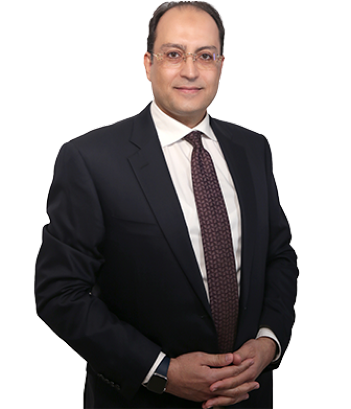 Dr. Mohamed Mashhour wearing a suit and tie stands with his hands folded